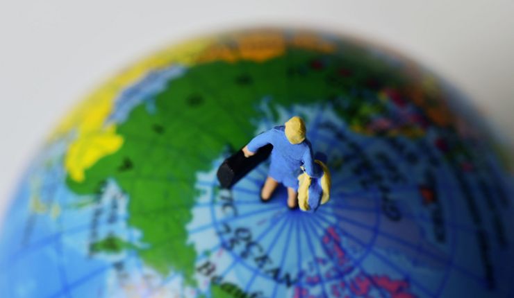 Draufsicht auf eine kleine Figur, die mit einem Koffer in der Hand auf einem Globus steht.